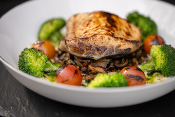 Grilled white fish fillet is laying on a bed of sauteed mushrooms and onions, garnished with blanched broccoli florets and grilled cherry tomatoes, creating a visually appealing and healthy meal