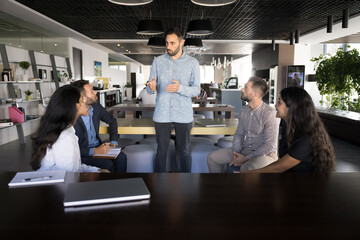 Young Hispanic man team leader, boss or staff member represent idea and work-related matter solution to employees colleagues at meeting in modern coworking office. Briefing event, brainstorm session