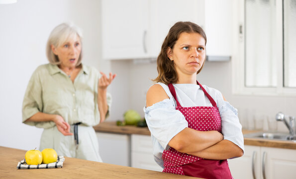 Senior woman scolding her adult daughter cooking breakfast in kitchen