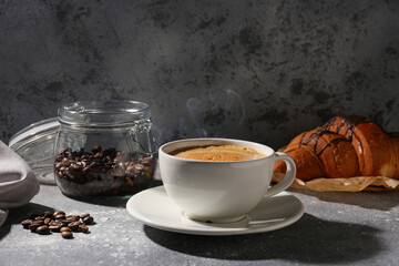 Cup of delicious espresso, coffee beans and croissant on table