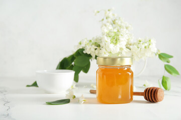 Bowl and jar of honey with flowers of acacia on light background, closeup