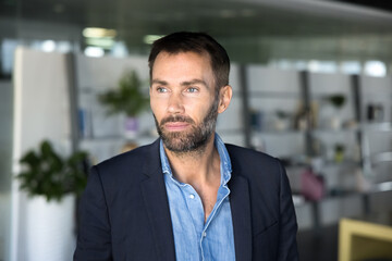 Fototapeta premium Mature European businessman dressed in suit looks aside thoughtfully, standing alone in workspace, reflecting on strategic decisions or work-related matters, exude leadership and authority, head shot