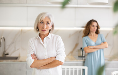 Adult woman gets angry during quarrel with elderly woman in kitchen