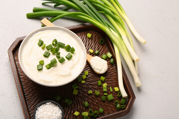 Tray with bowl of tasty sour cream and sliced green onion on white background
