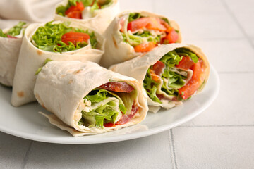 Plate of tasty lavash rolls with tomatoes and greens on white tile background
