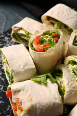 Board of tasty lavash rolls with vegetables and greens on black background, closeup