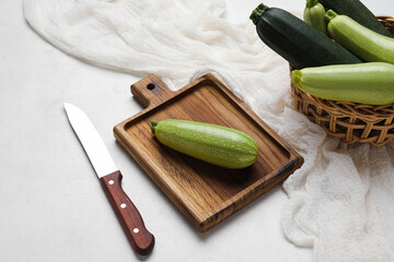 Wooden board and wicker basket with raw zucchini on light background