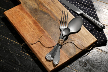 New cutting board, spoons and fork on black wooden background