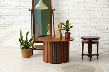 Brown wooden coffee tables with floor mirror and houseplants near white brick wall