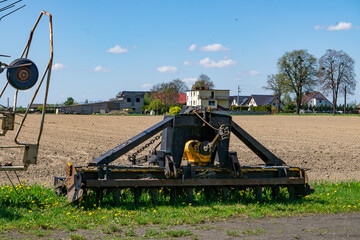 Fototapeta premium An agricultural machine stands on the edge of a field in a rural landscape. Single-family homes and trees are visible in the background.