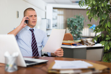 Male clerical worker having telephone conversation during his work day in office.