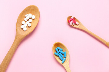 Wooden spoons with different pills on pink background