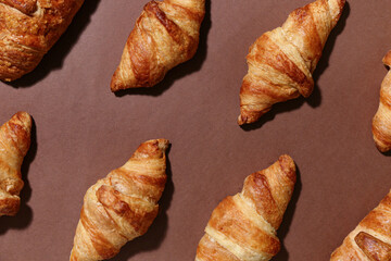 Many tasty croissants on brown background