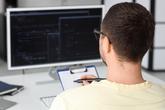 Male programmer with clipboard in office, back view