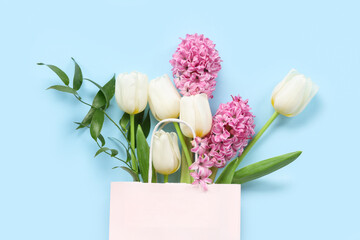 Paper shopping bag with flowers and green twigs on blue background