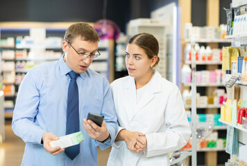 Obraz premium Male buyer together with female pharmacist scans QR code on medicine label in pharmacy