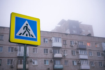 Pedestrian crossing sign on the background of an old multi-storey building with windows and balconies on a foggy rainy gray morning