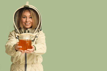Female beekeeper with jar of sweet honey and dipper on green background