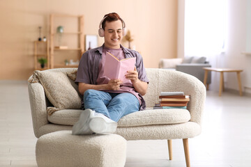 Young man listening music and reading book on sofa in living room