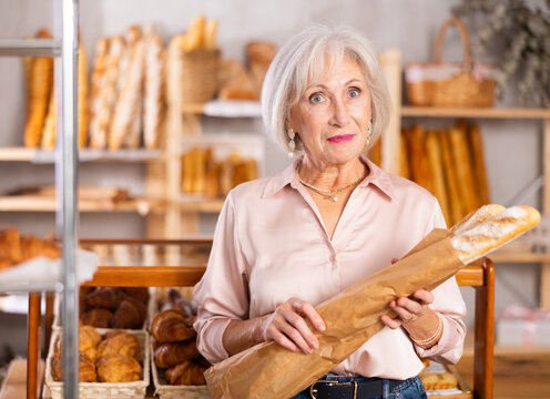 Mature female shopper with paper bag of fresh bread and baguettes in bakery