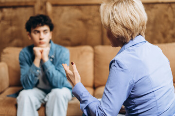 Psychotherapist talking to troubled teenage boy sitting on couch