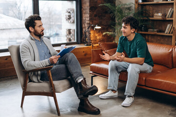 Smiling teenage boy talking with male psychoanalyst during therapy session