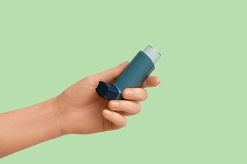 Female hand with modern asthma inhaler on green background
