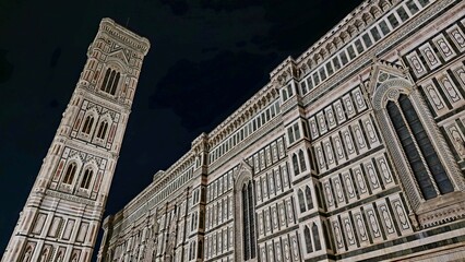 Florence, Italy - 4 January 2025. Night view of Florence Cathedral’s side wall and Giotto’s Campanile, both lit to reveal detailed marble patterns and Gothic windows.