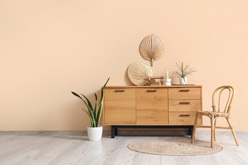 Wooden cabinet with decor and houseplant near beige wall