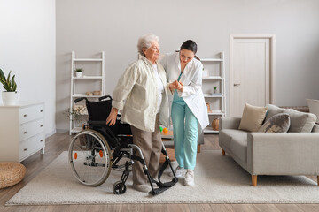 Physical therapist helping senior woman to stand up from wheelchair at home