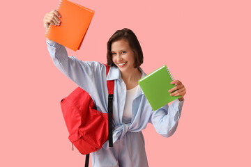 Beautiful female student with backpack and notebooks on pink background