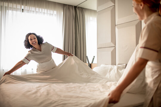 Hotel housekeeping staff making bed with clean linens in bright room