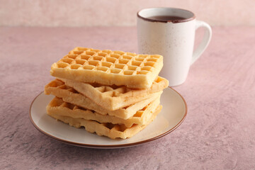 Plate with delicious Belgian waffles and cup of tea on pink background