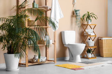 Interior of modern restroom with white toilet bowl, braided basket and shelving unit near beige wall