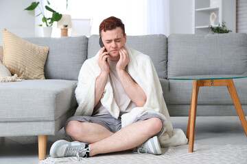 Young man talking with mobile phone and suffering from toothache in room
