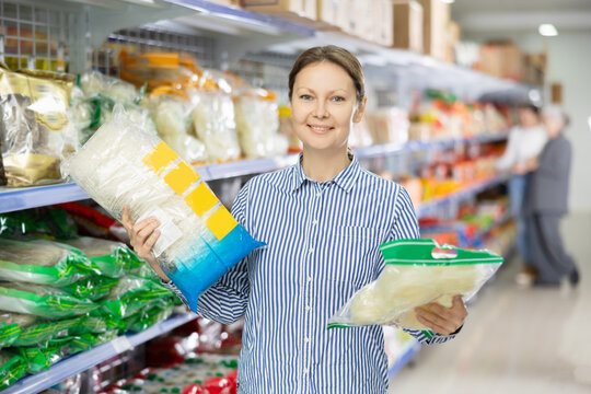 Middle-aged woman in shop carefully examines information about product on label packaging. Female customer chooses and buys pack of Chinese noodles at hypermarket