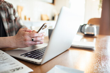 Close up of man paying bills online using smartphone and laptop at kitchen table