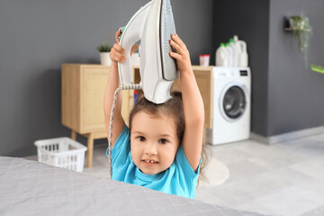 Cute little girl taking iron from board in bathroom. Child at risk