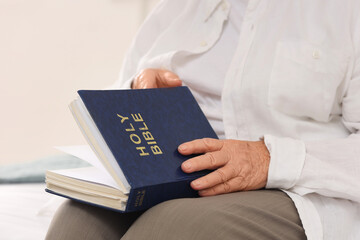 Senior woman with Bible sitting on bed at home, closeup
