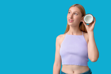 Beautiful young happy woman in stylish summer outfit with half of coconut on blue background