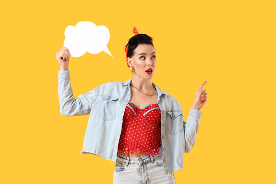 Young pin-up woman with blank speech bubble pointing at something on yellow background