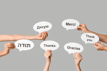 Female hands holding speech bubbles with text THANK YOU in different languages on grey background