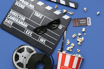 Movie clapper with cinema ticket, glasses, popcorn and film reels on blue background