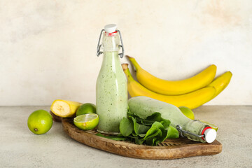 Bottles of fresh spinach smoothie with limes and bananas on white background