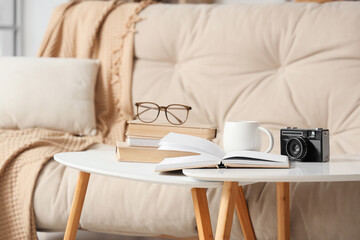 Books with eyeglasses, tea cup and photo camera on tables in living room, closeup