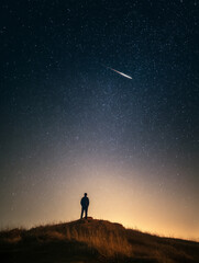 Fototapeta premium Night sky photography of man watching meteor shower on hill under starry sky landscape astrophotography