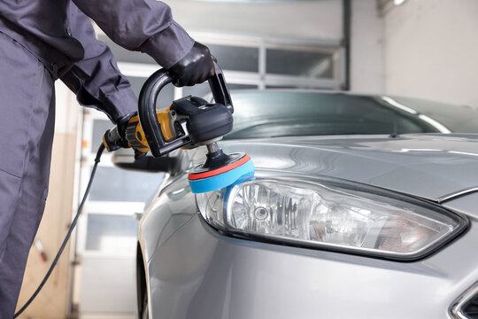 Man polishing car headlight with orbital polisher indoors, closeup