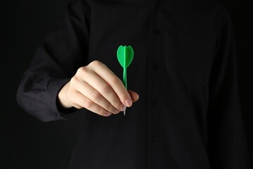 Woman holding dart on black background, closeup