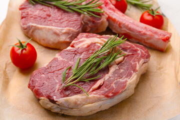 Pieces of raw beef, rosemary and tomatoes on parchment, closeup