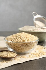 Brown rice, flour and sieve on grey table, closeup. Space for text